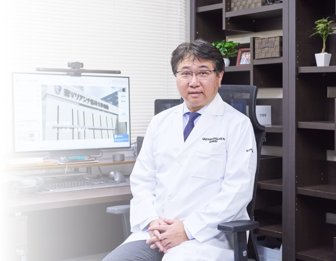 執務室で椅子に座りこちらを見る民上教授